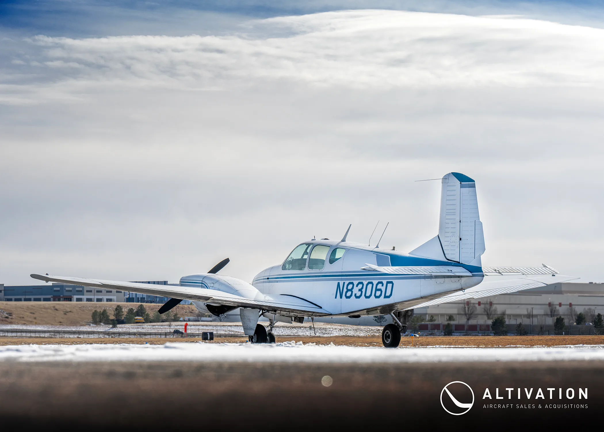A white and blue twin-engine aircraft with registration N8306D is parked on a tarmac, viewed from the side.