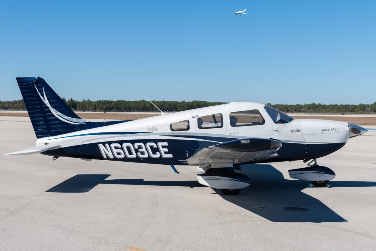 Side view of the Piper Archer LX N603CE on the tarmac with another aircraft in the sky.