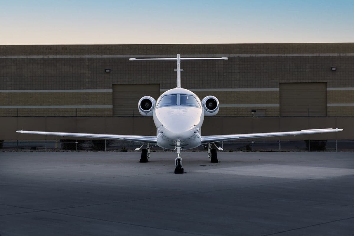 A head-on view of a white business jet with gold and black stripes, tail number N390DP, parked on an airport tarmac.