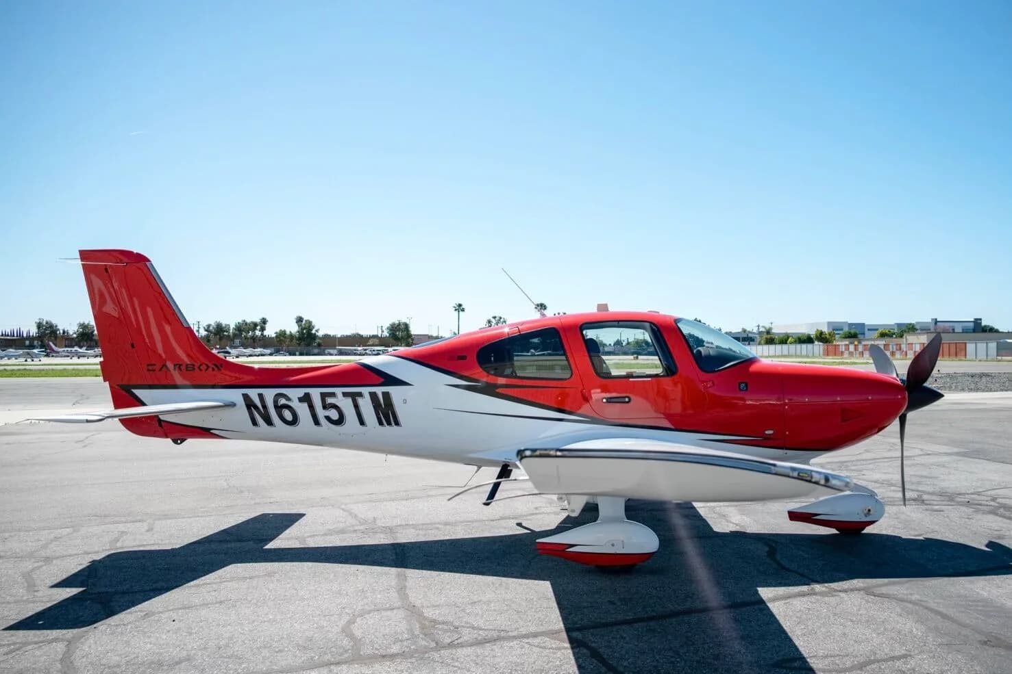 Side view of a red and white N615TM aircraft with its doors closed, parked on an airfield.