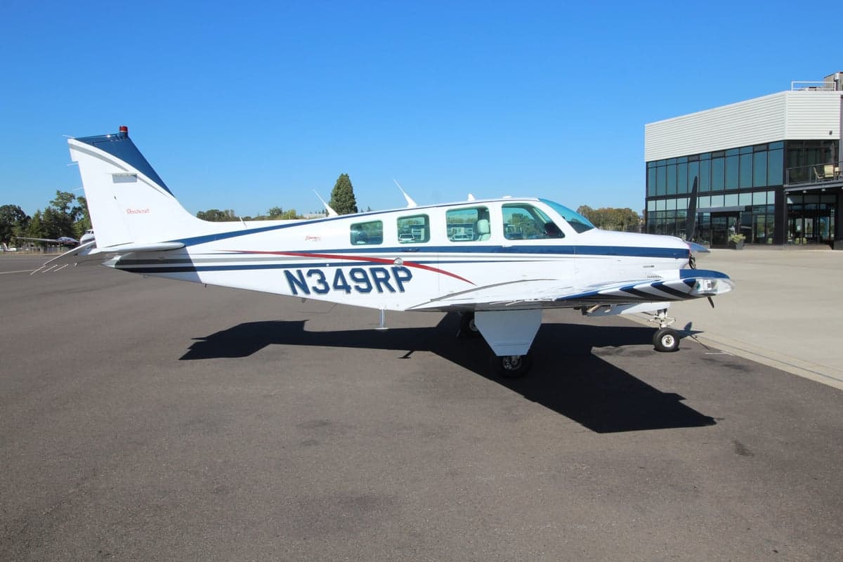 A Beechcraft Bonanza is parked on the tarmac on a sunny day.