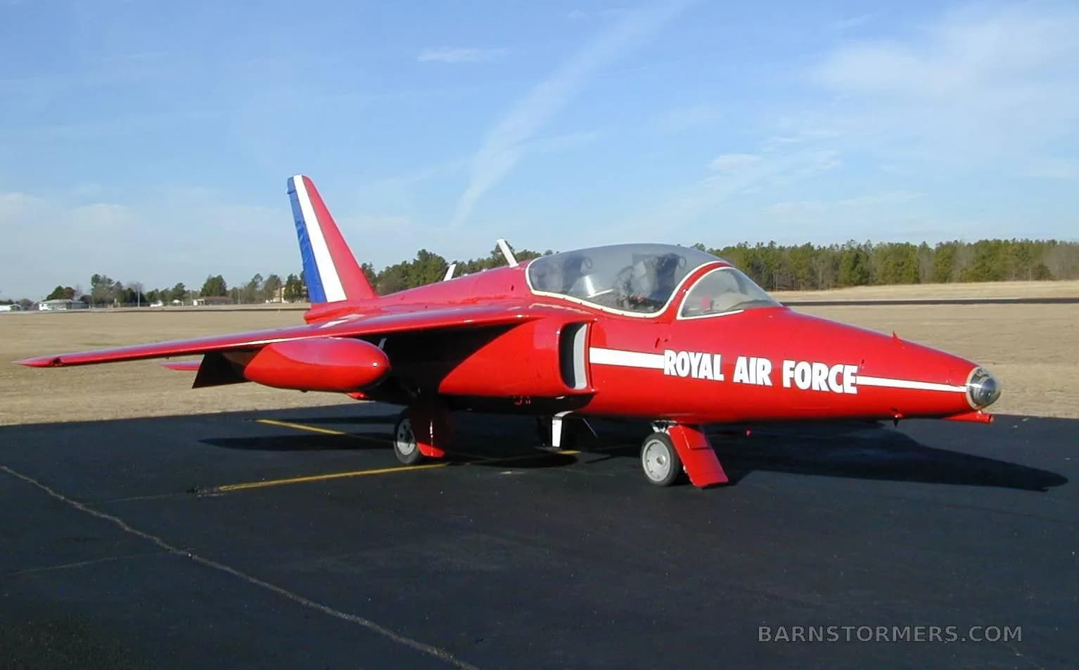 A red jet aircraft with 'ROYAL AIR FORCE' painted on its side, parked on an asphalt runway under a clear sky.