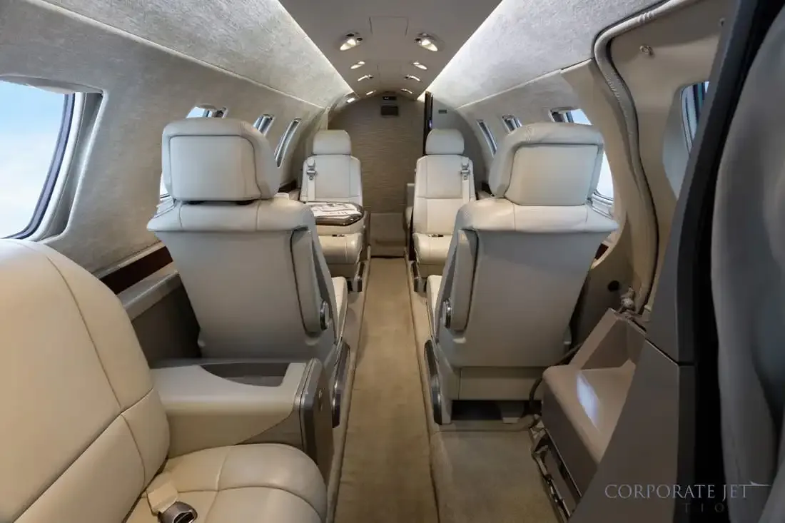 The interior of a private jet cabin with light-colored leather seats, viewed from the front looking back.