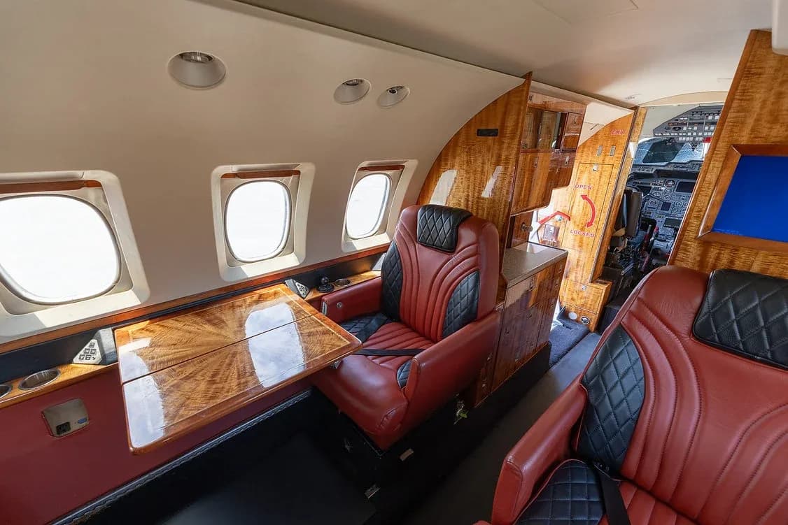 Two red and black leather seats in the private jet's cabin, with a polished wood table extended between them.