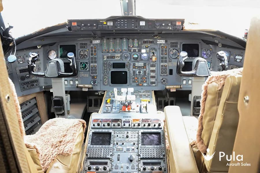 The cockpit of a Bombardier Challenger 604 (N64JS) with multiple screens, gauges, and controls.
