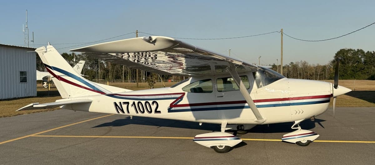 Side view of the Cessna 210 Centurion N71002, showcasing its white paint scheme with blue and maroon accents.
