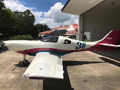A white and pink aircraft with the number 38 on the side is parked in front of a hangar.
