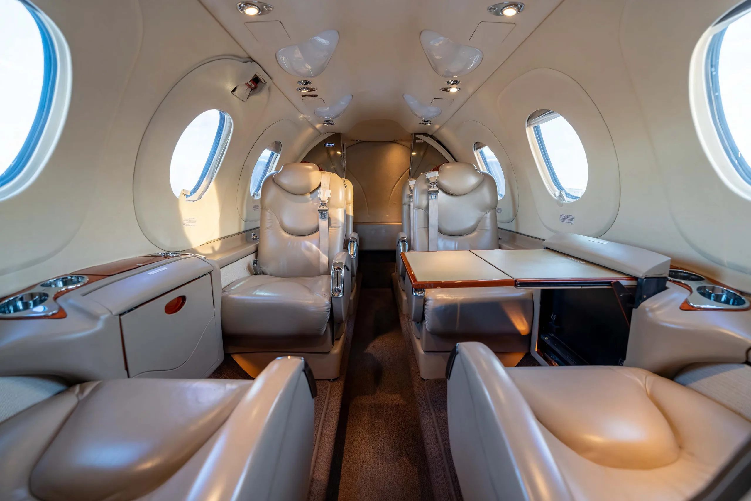 The interior cabin of a business jet with light tan leather seats arranged in a club configuration and small tables.