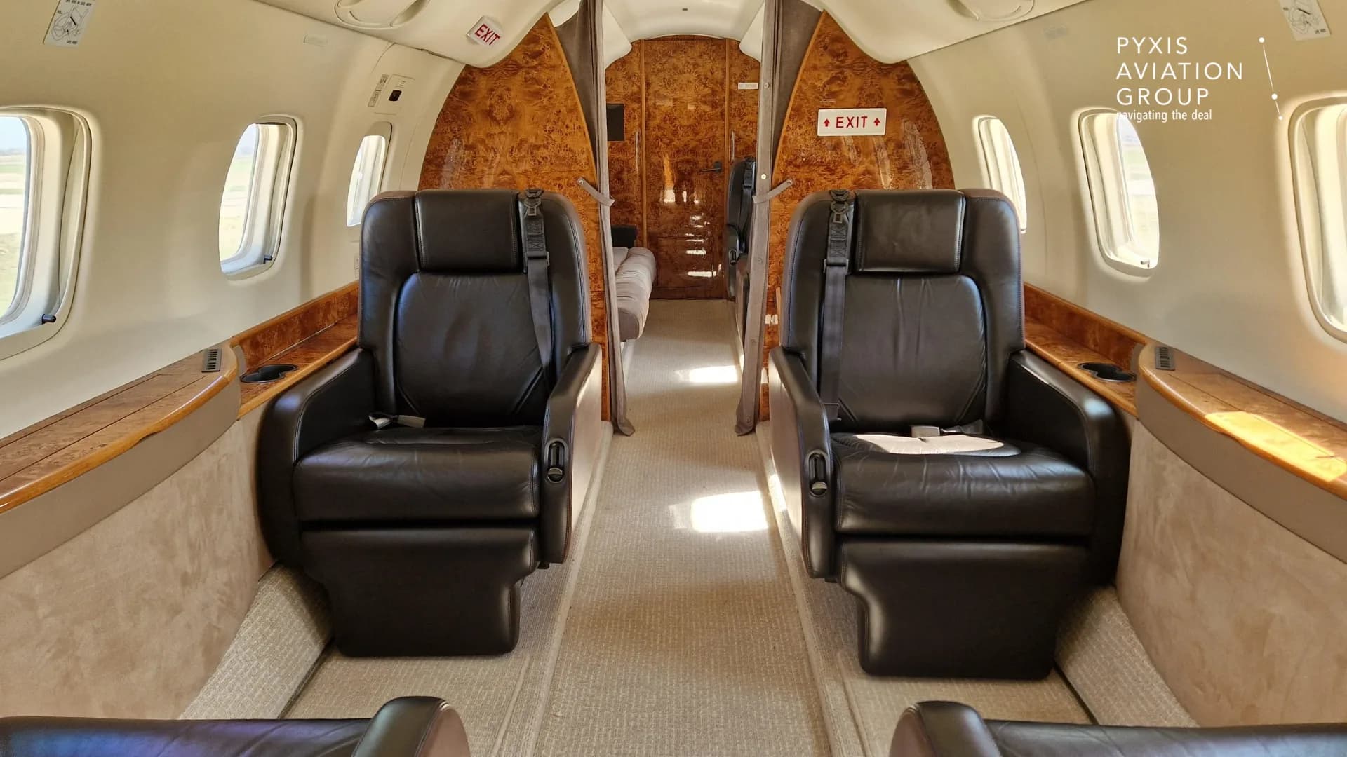 A view of the aircraft cabin interior with two dark leather seats in the foreground and wood paneling.