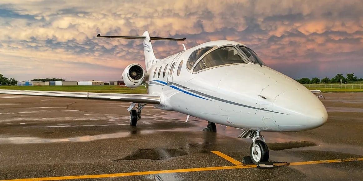 Front view of a white jet aircraft on the tarmac with a dramatic sky in the background.