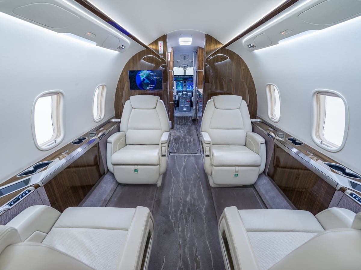View of the aircraft's interior with white leather seats and wood trim.