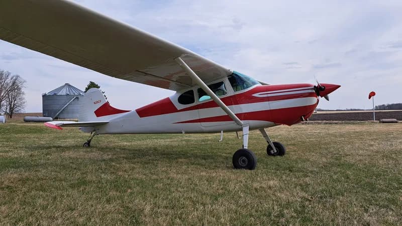 Side view of a red and white Cessna on a grassy field.