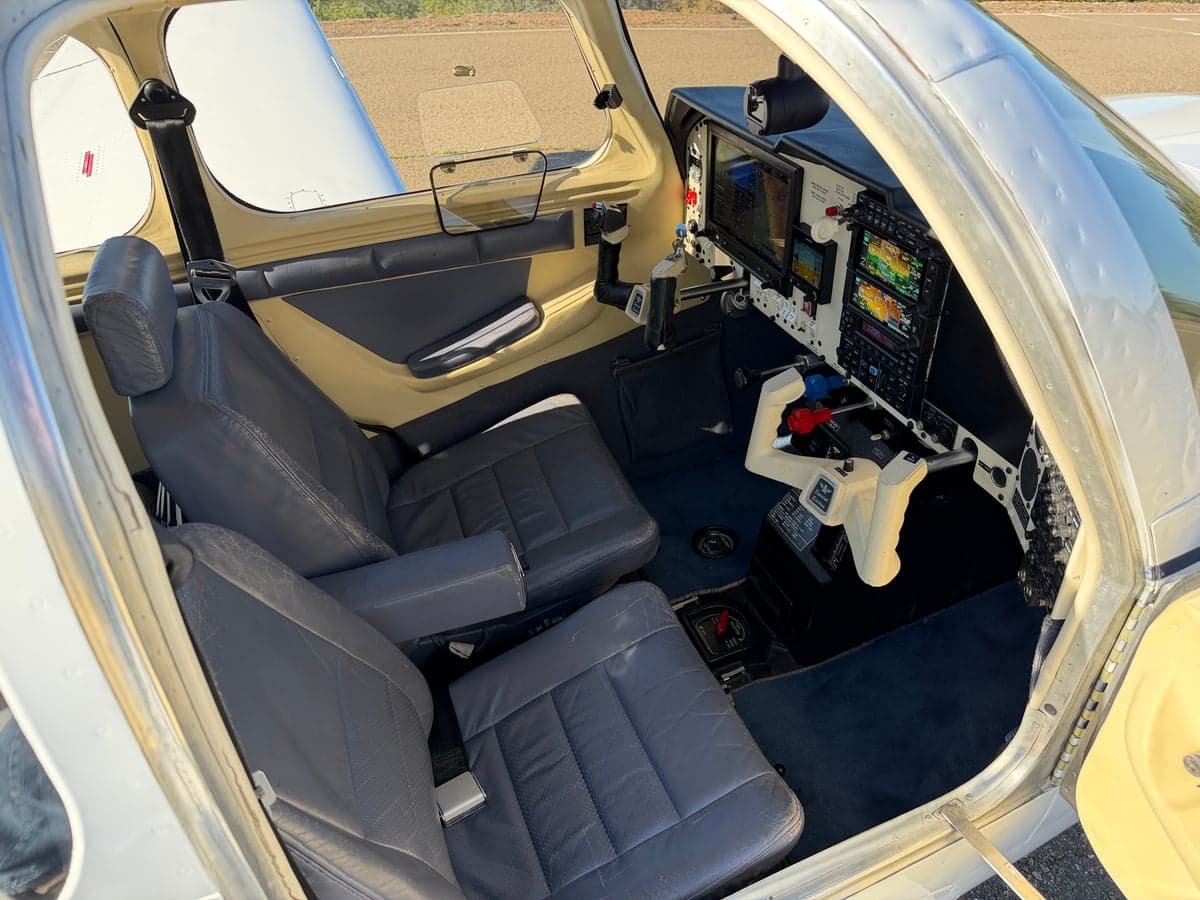View of the front seats and cockpit of the Mooney M20J from the open doorway.