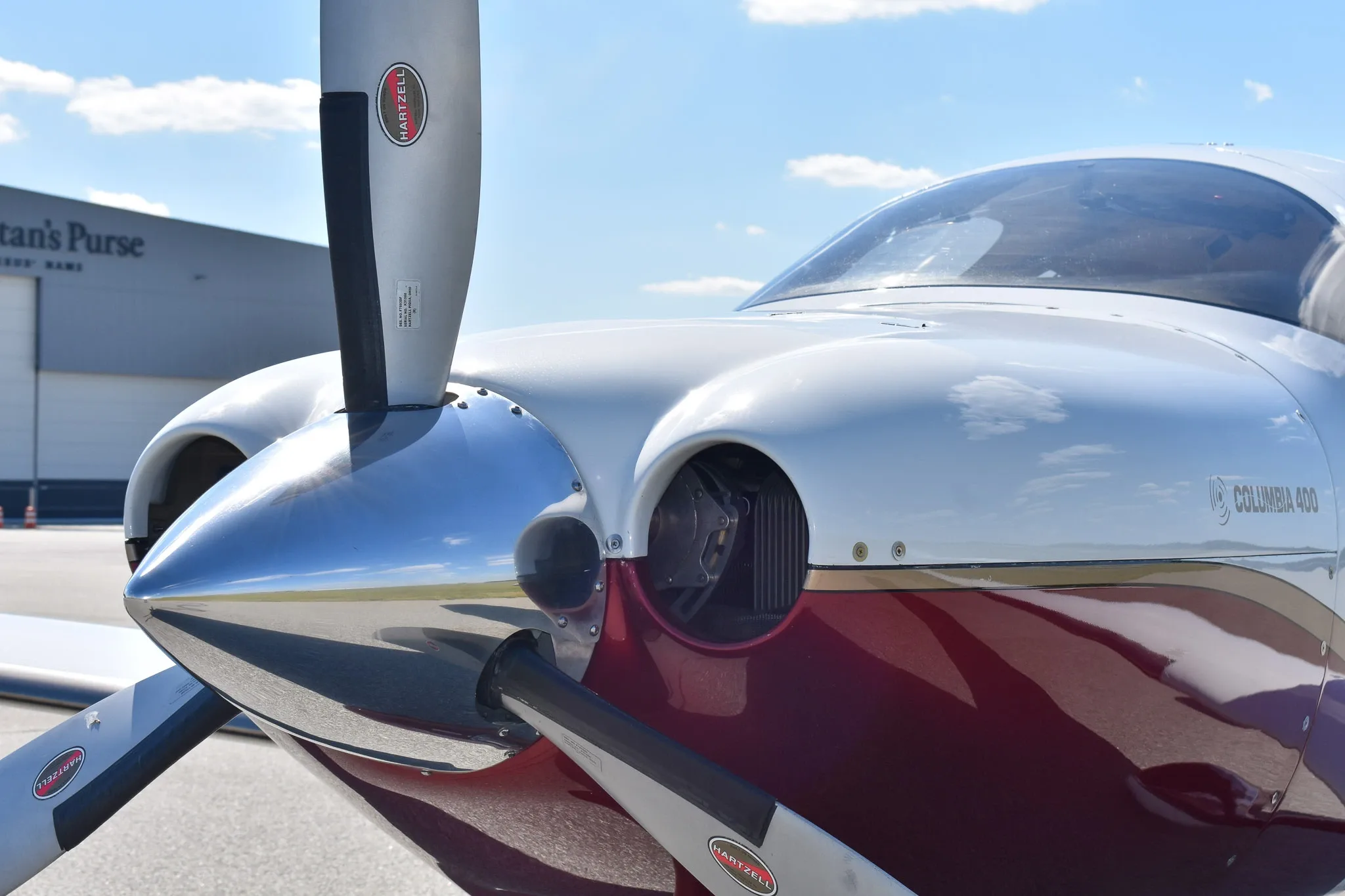 Close-up of the propeller and nose of a white and maroon Columbia 400 aircraft.