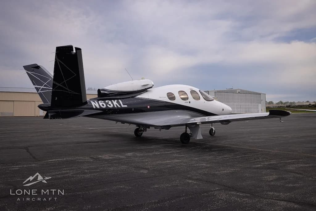 A rear three-quarter view of a white and black Cirrus Vision Jet (N63KL) parked on an asphalt apron.