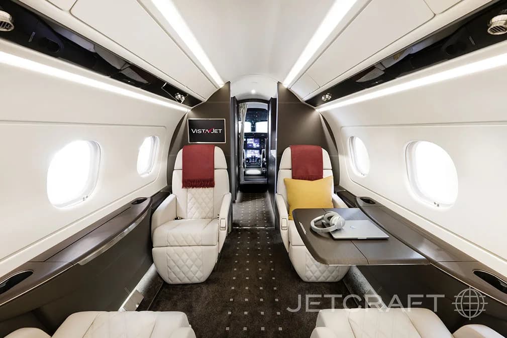 The interior of a jet aircraft with white leather seats and a table with a laptop and headphones.