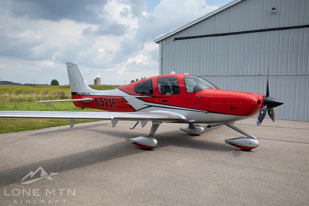 A red and silver Cirrus SR22 aircraft, N521P, parked on an asphalt ramp in front of a hangar.