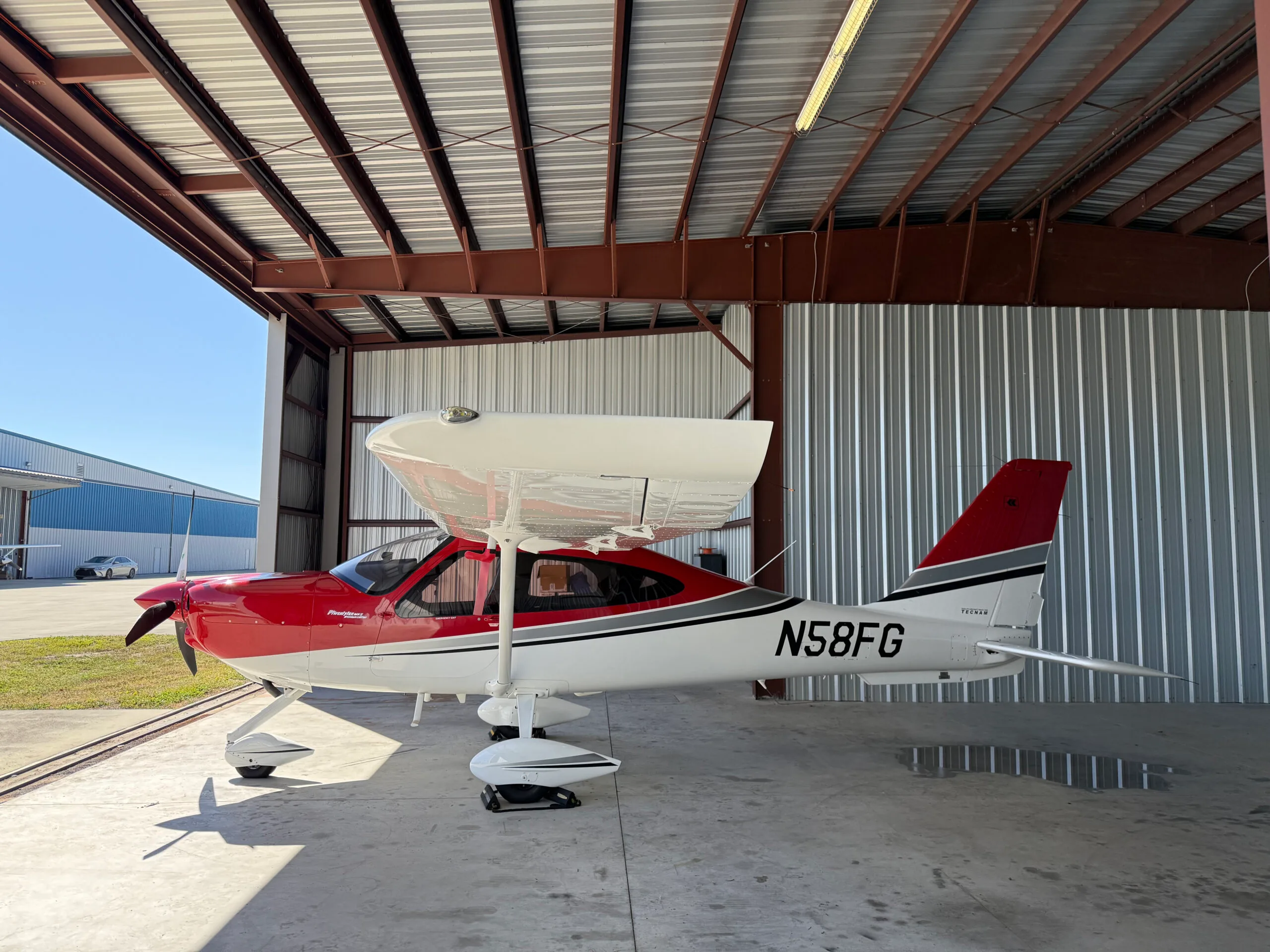 Tecnam P2010 aircraft N58FG parked in a hangar with a red and white paint scheme.