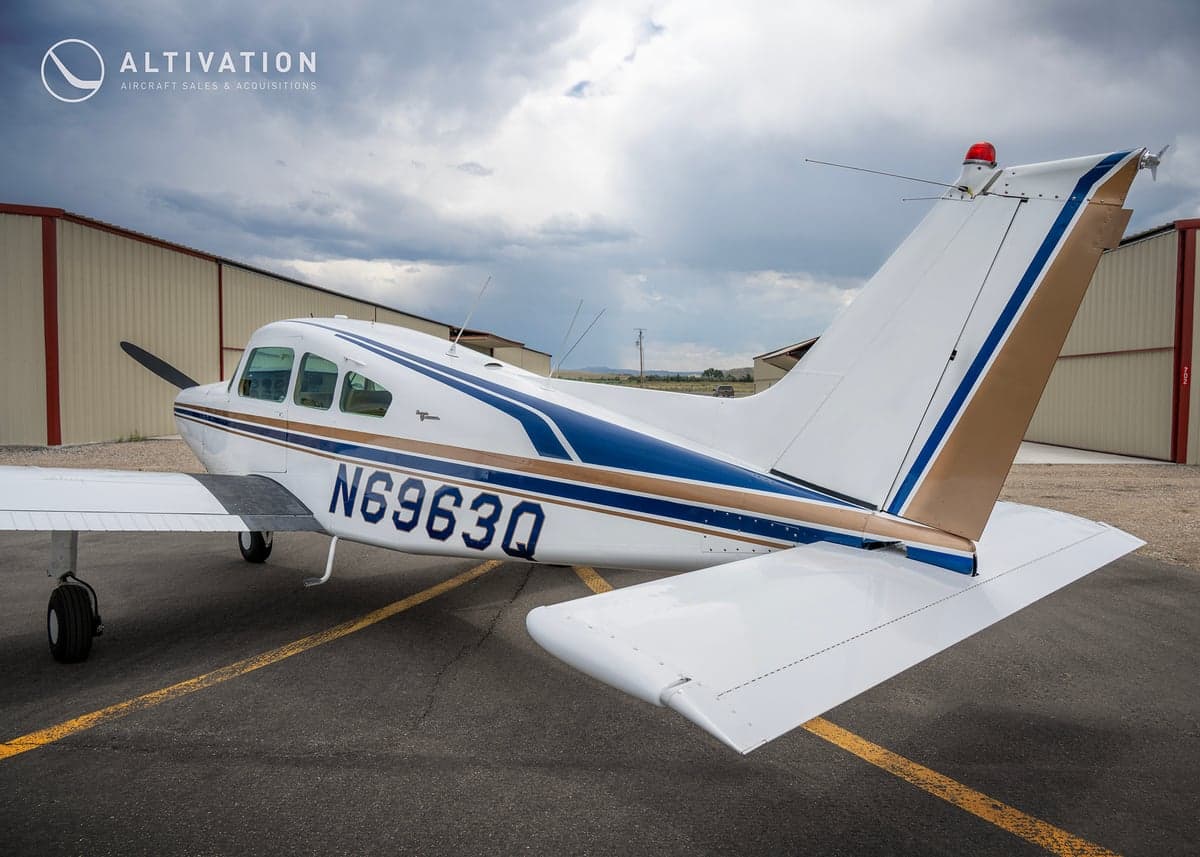 Side and rear view of a white and blue Piper aircraft showing the tail and registration number.