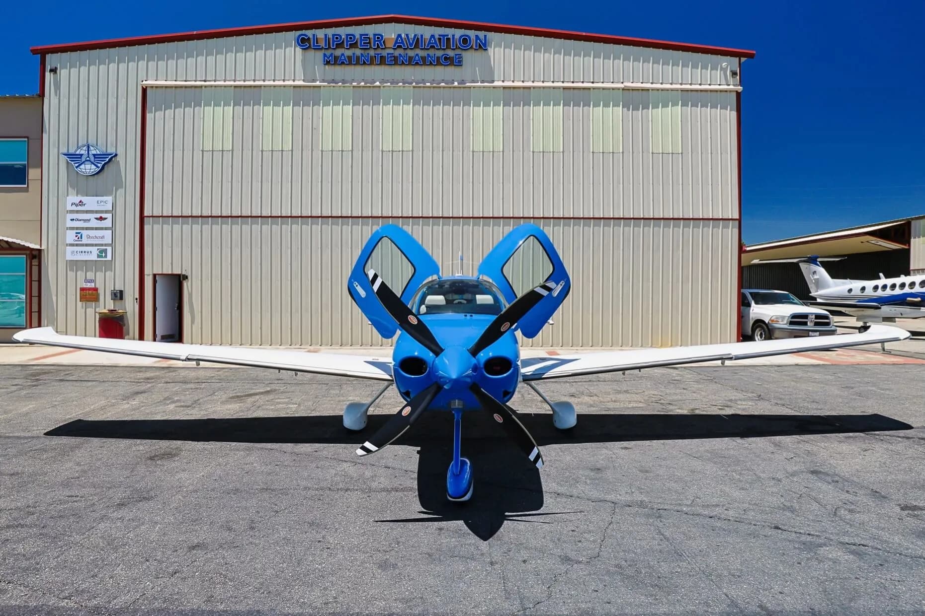 Front view of a blue and white Cirrus SR22 aircraft (N99W) with open doors, parked in front of a hangar.