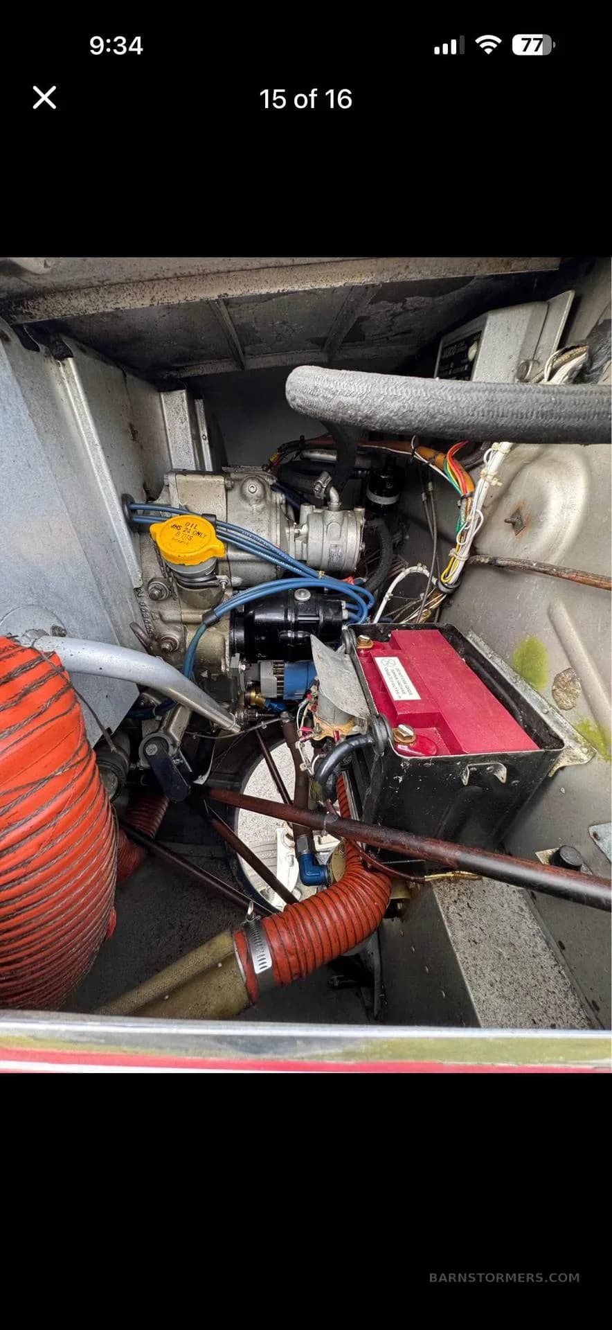 A detailed view of an aircraft engine compartment, showing the engine, red battery, and various components.