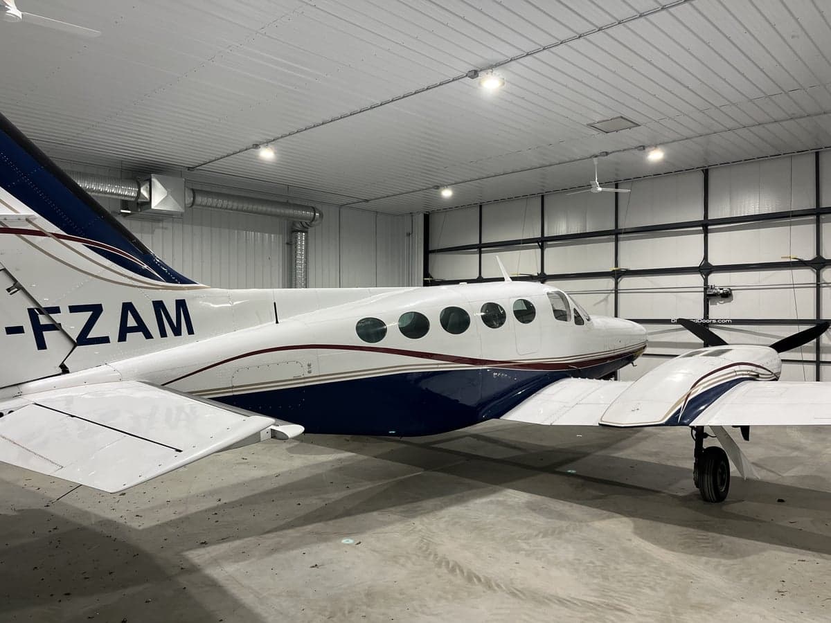 A white and blue twin-engine aircraft is parked in a hangar.