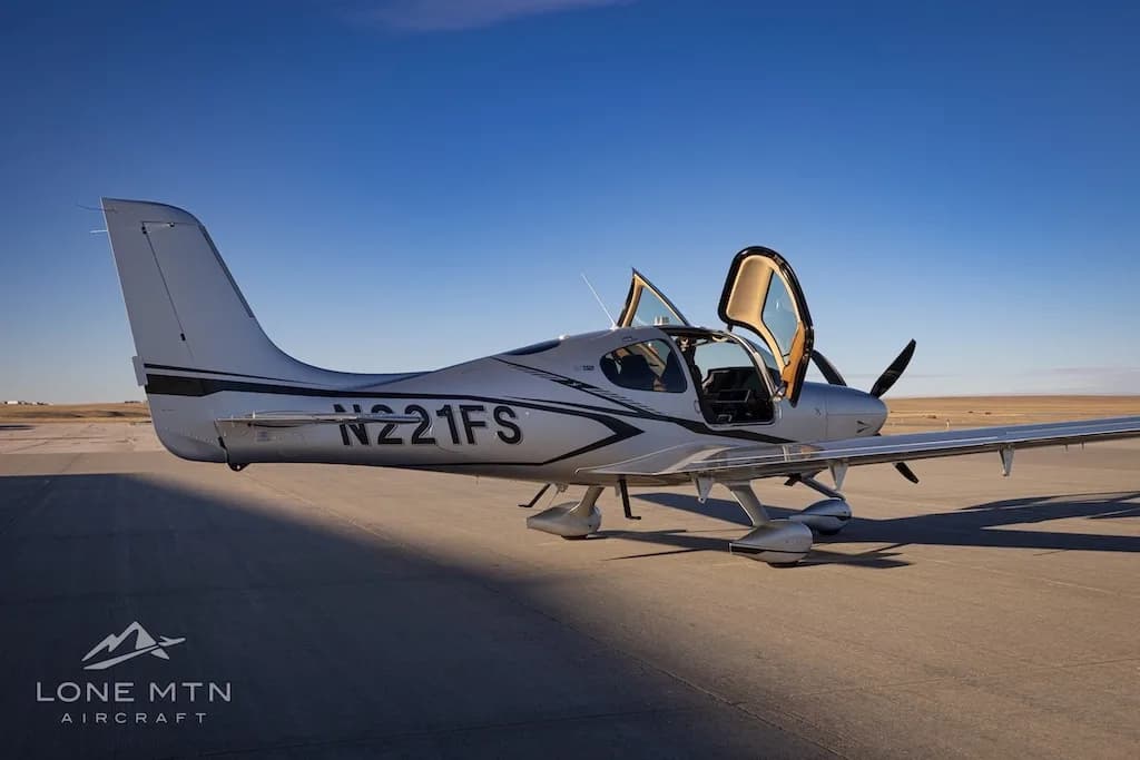 A side view of the silver Cirrus SR22T aircraft N221FS with its doors open, parked on an airfield.