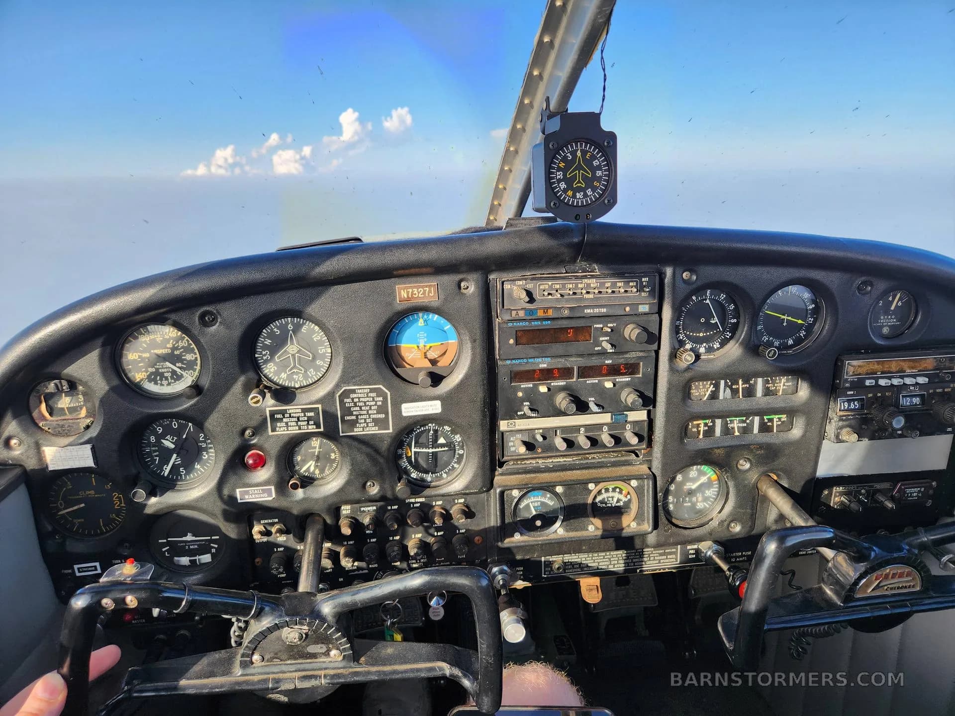 The instrument panel and controls of a Piper Cherokee aircraft, with a view of clouds outside the windshield.