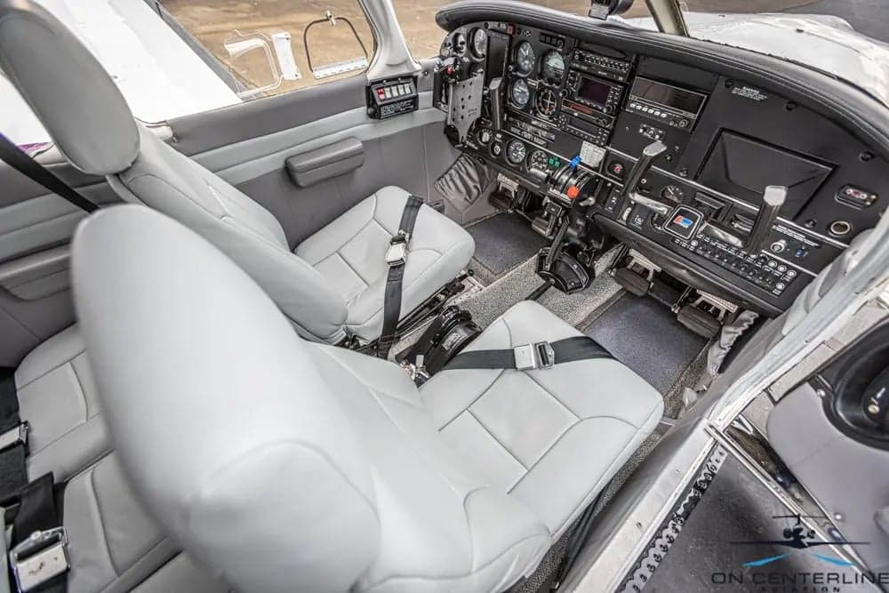 View of the cockpit of a Piper PA-32R-301 Saratoga SP, featuring gray seats and a black instrument panel.