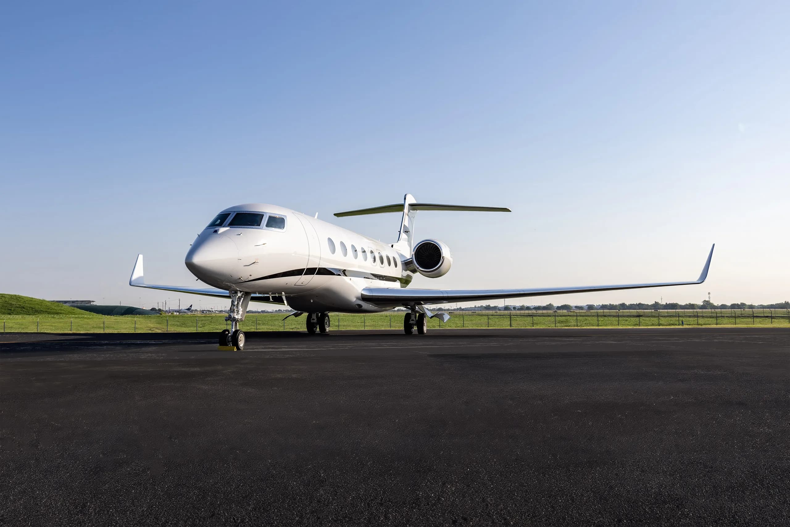 A sleek white Gulfstream G650 business jet is parked on an airport tarmac under a clear blue sky.