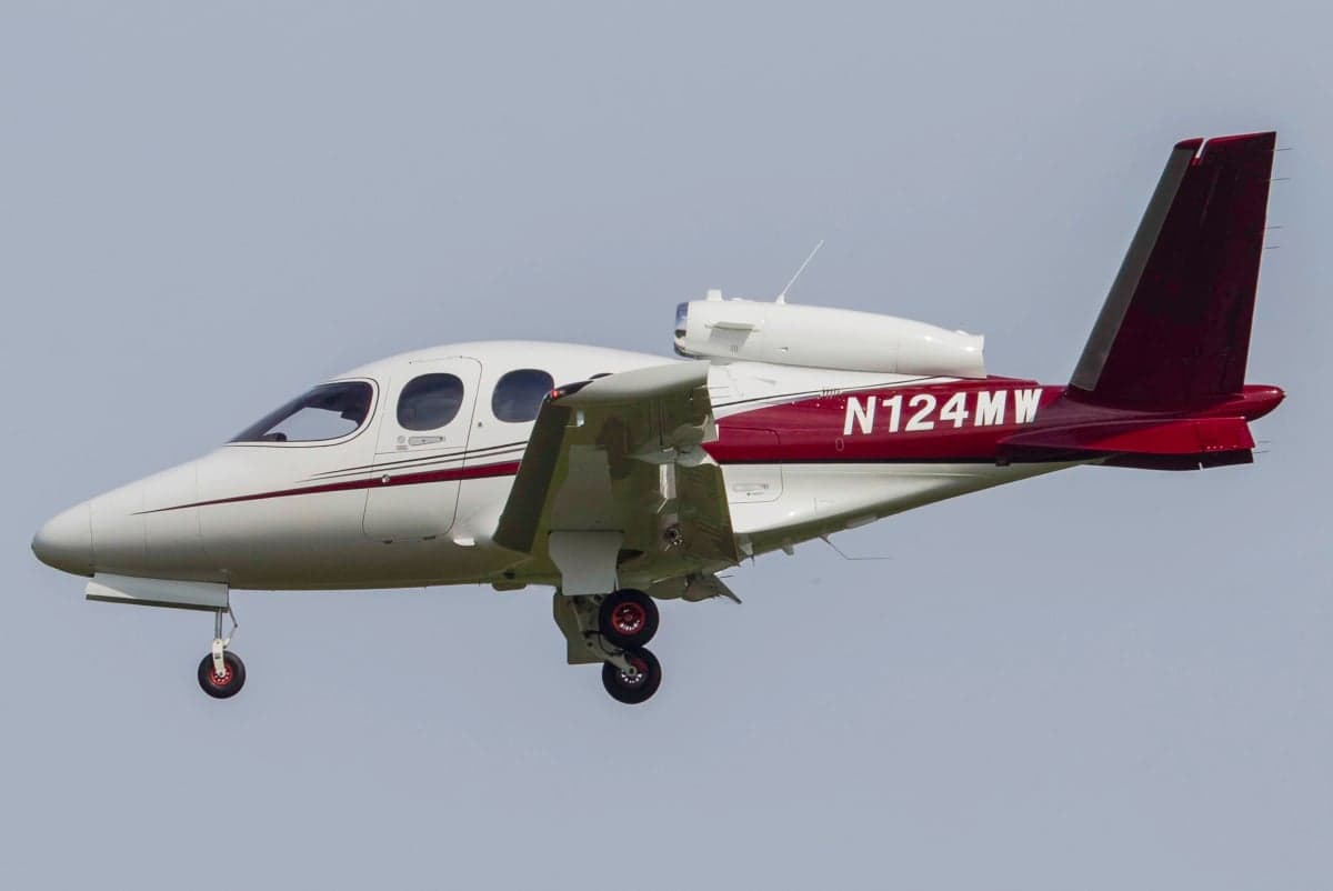 A white and red Cirrus Vision Jet, tail number N124MW, is shown in flight against a clear sky.