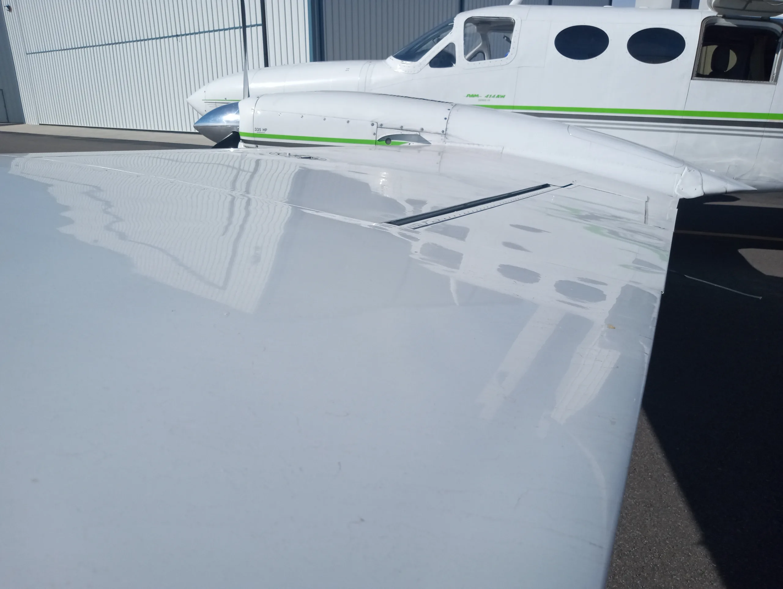 A close-up view of the white wing and fuselage of a twin-engine aircraft with green and black stripes.