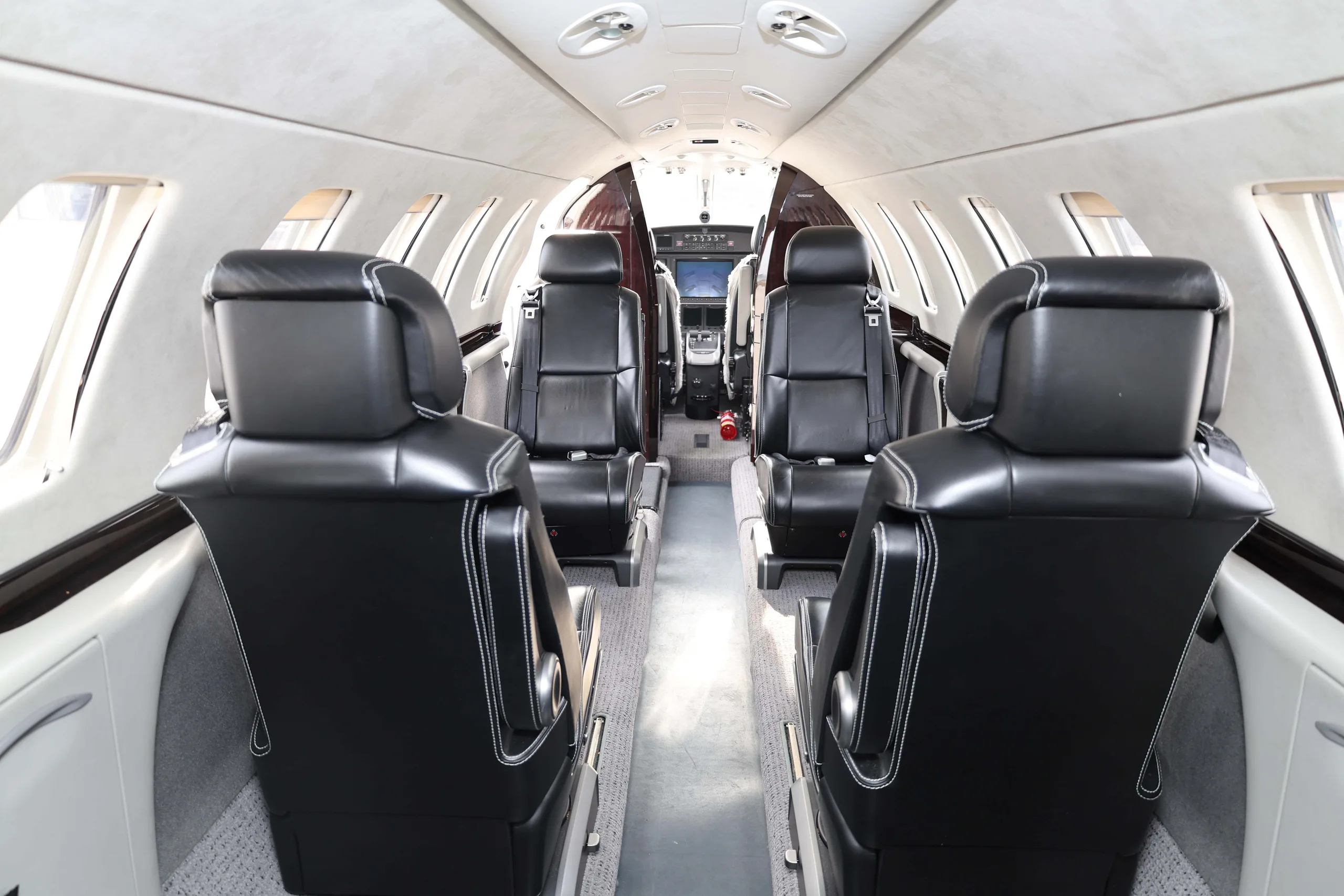 The interior cabin of a business jet, showing black leather seats and a view towards the cockpit.