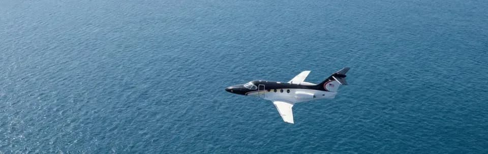A black and white Hawker 400XP flying over the ocean.