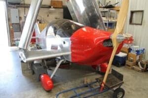 Front view of a red and silver aircraft with its engine compartment open in a hangar.