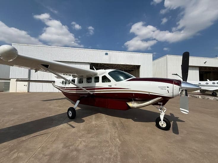 A maroon and white Cessna Caravan parked in front of a hangar.