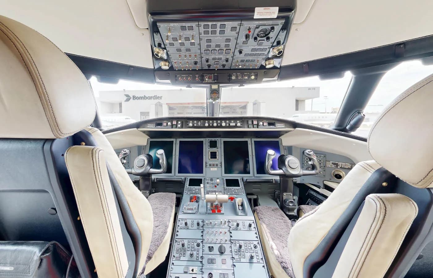 The cockpit of a Bombardier Challenger jet features multiple screens, control panels, and two pilot seats.