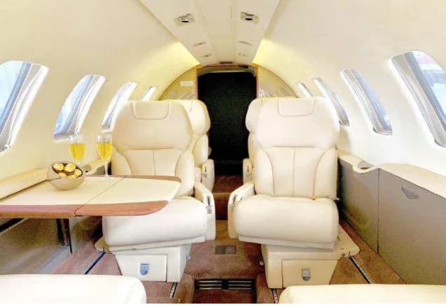 Interior view of aircraft cabin with two cream-colored leather seats and a table with refreshments.