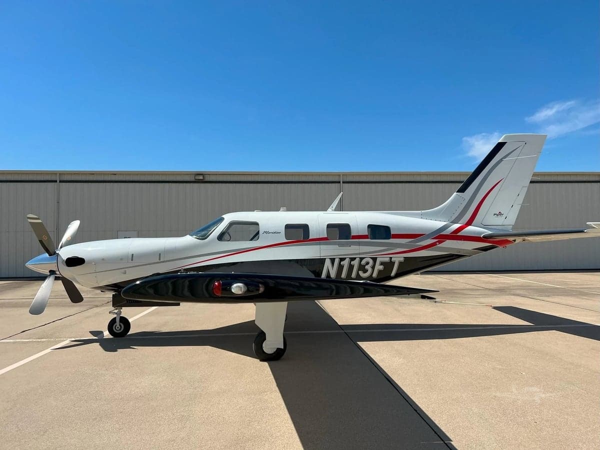 Side view of a Piper Meridian aircraft with a white, black, and red paint scheme parked on the tarmac.