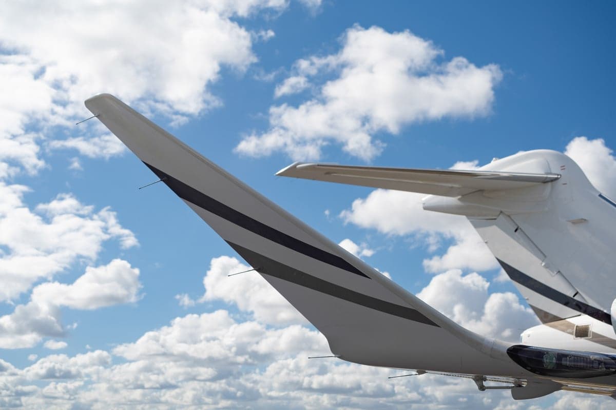 A view of the white tail and horizontal stabilizer of a business jet with dark stripes against a cloudy blue sky.
