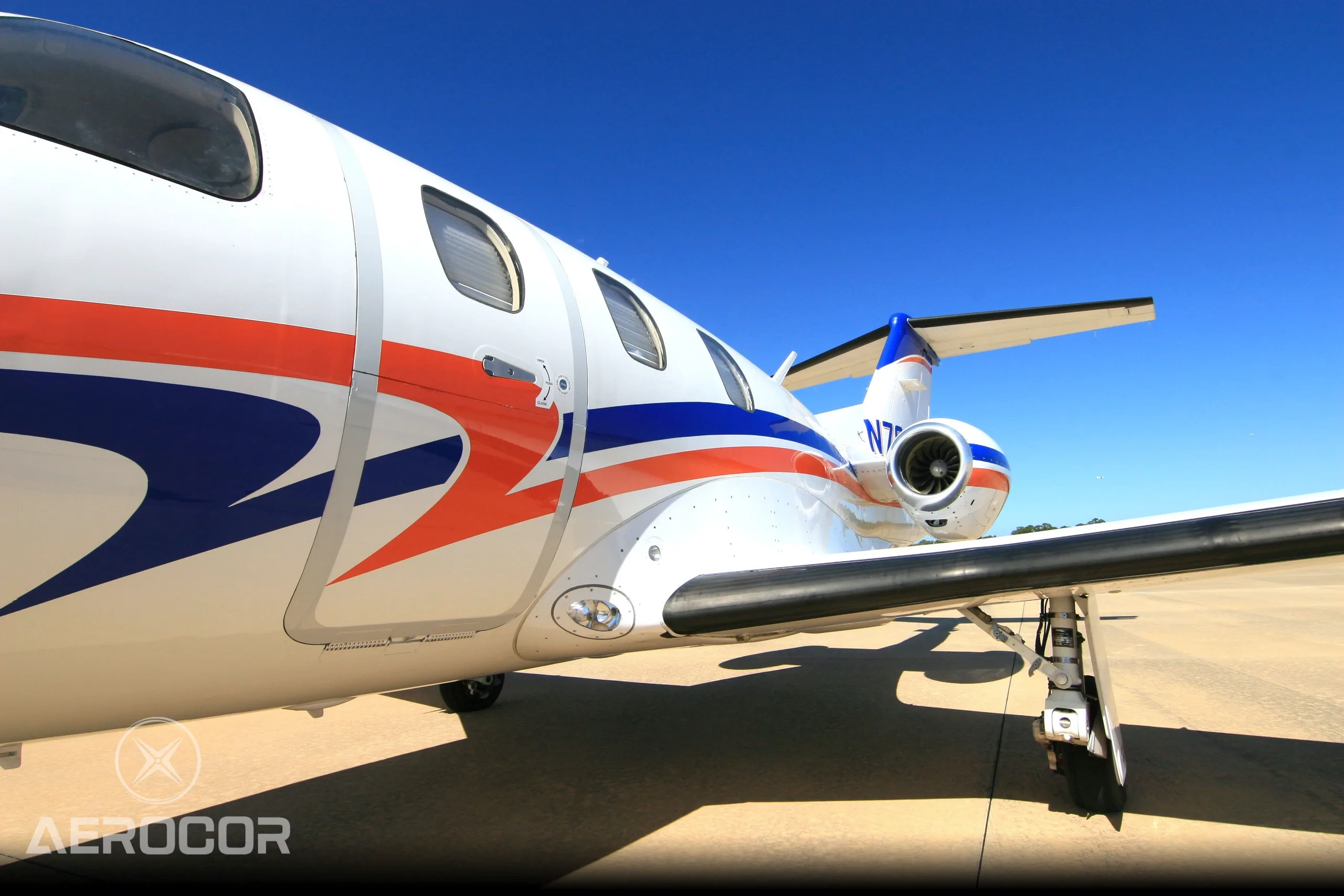 A close-up side view of the fuselage and engine of a white Eclipse 500 jet with blue and orange stripes, tail number N703BR.