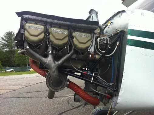 The engine of a white and green aircraft is exposed for maintenance.