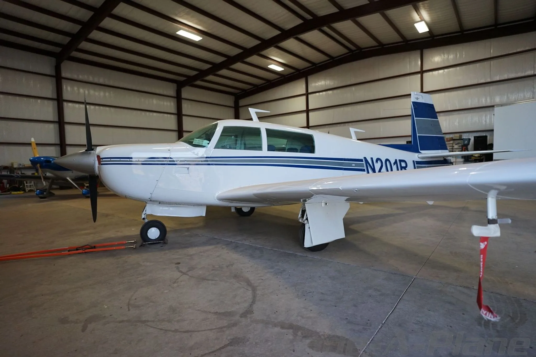 A side view of the white single-engine aircraft N201RJ with blue and grey stripes, parked in a hangar.