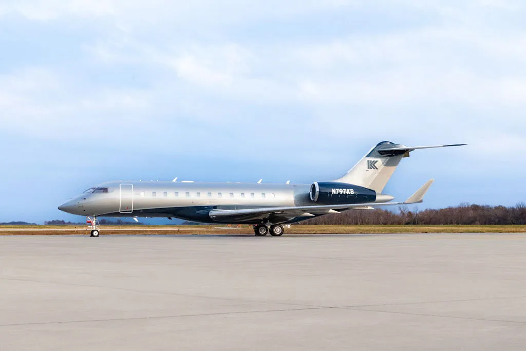 A side view of the N797KB Bombardier Challenger business jet in silver and blue on a tarmac.
