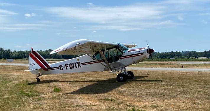 A Super Cub aircraft with registration C-FWIX is parked on a grassy field.