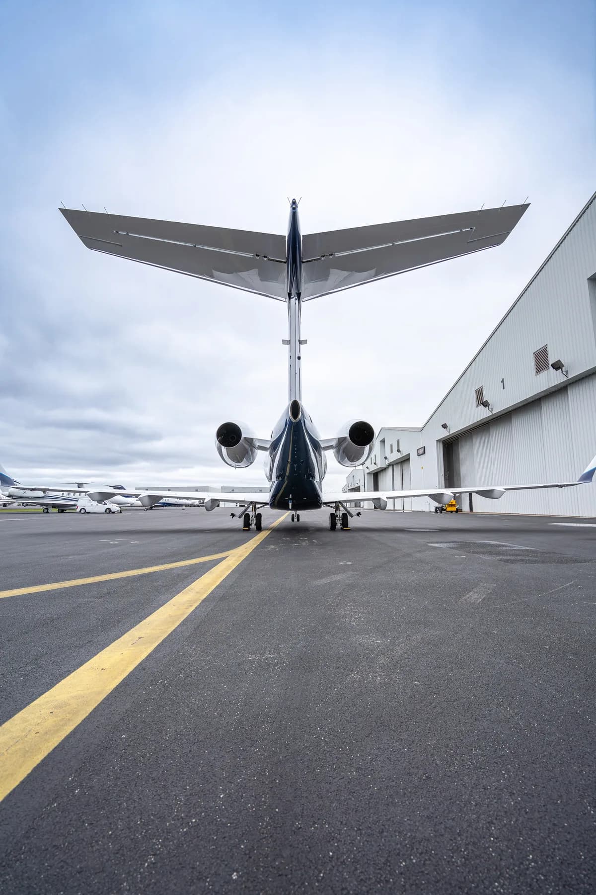 A rear view of a private jet with a dark blue tail and engines, parked on an airport tarmac.