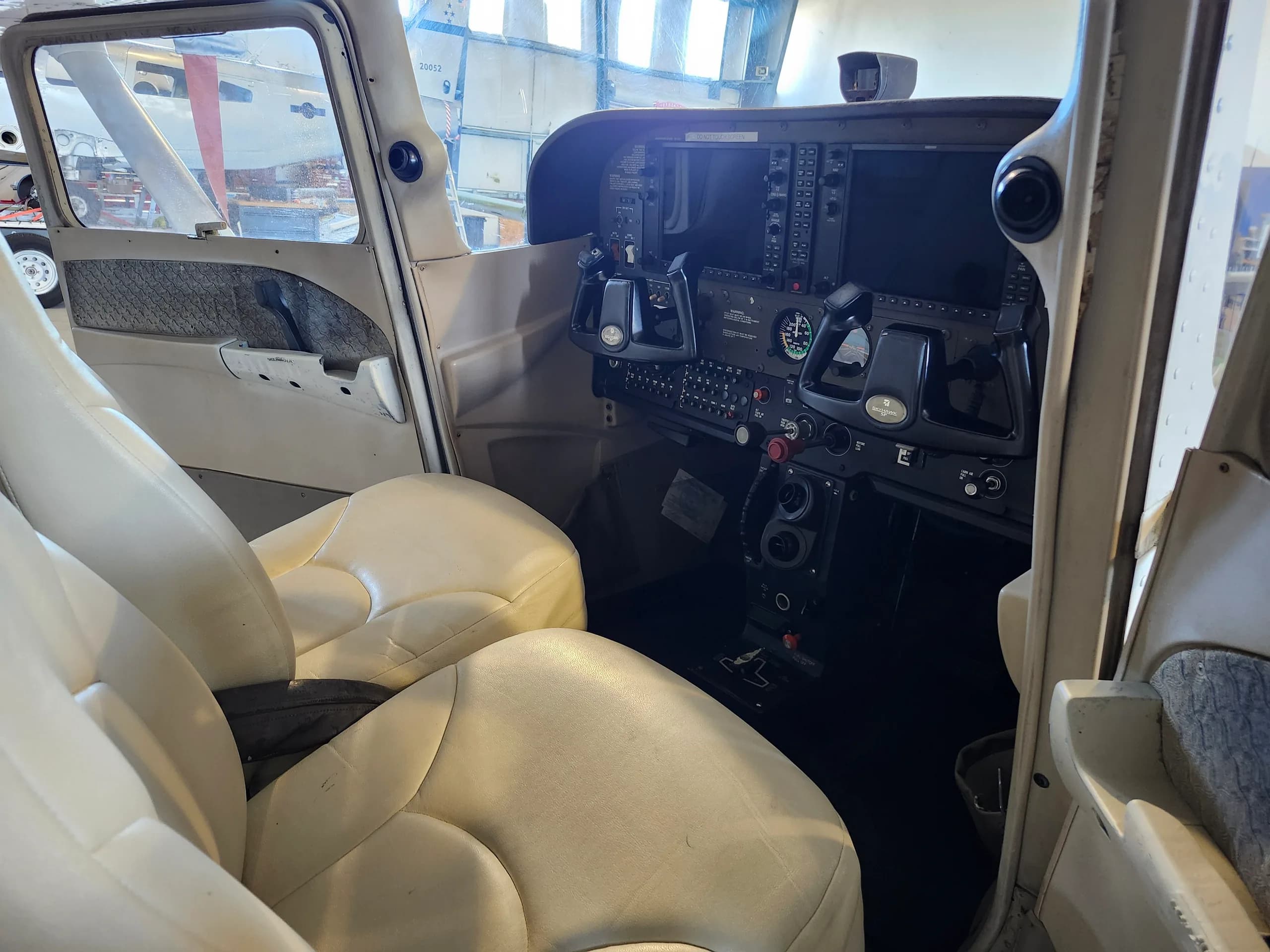 Interior view of the aircraft cabin with beige seats and a partial view of the cockpit.