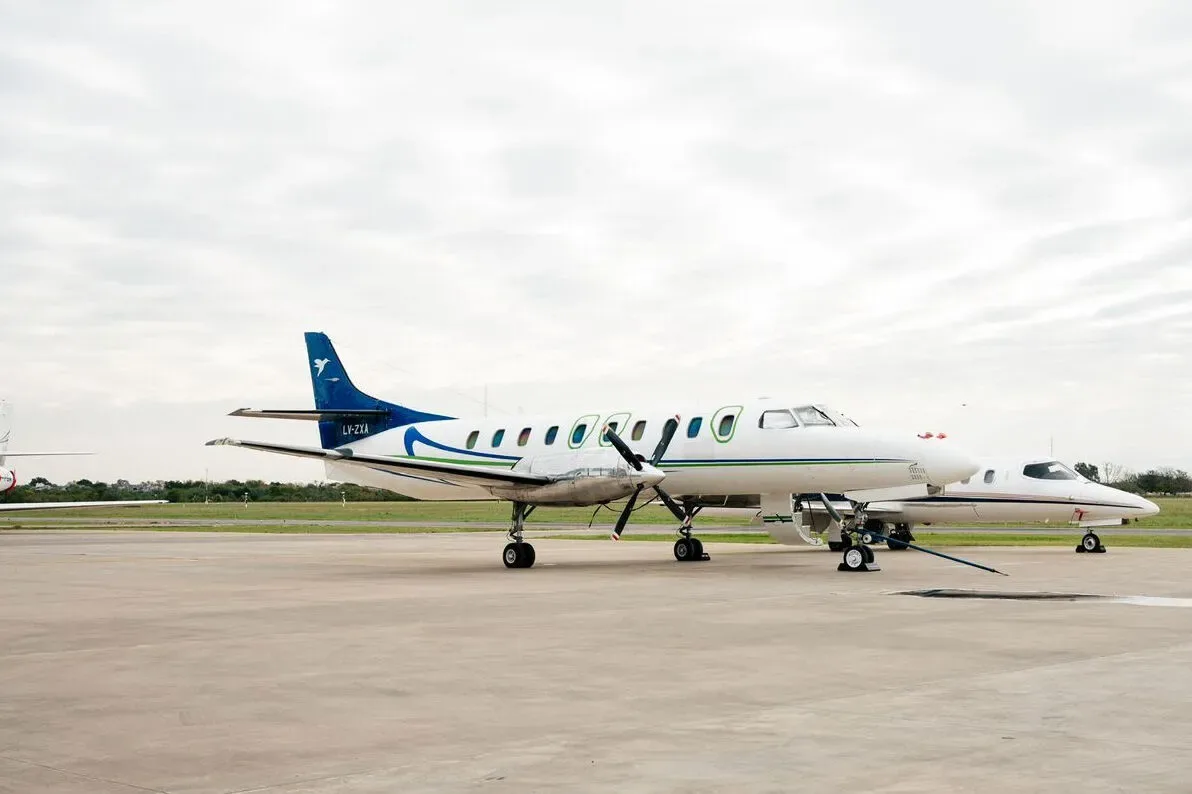 A white turboprop aircraft with blue and green stripes on the tail and fuselage, parked on an tarmac next to a smaller white jet.