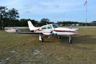 A white and maroon Beechcraft Baron is parked on a grassy field.