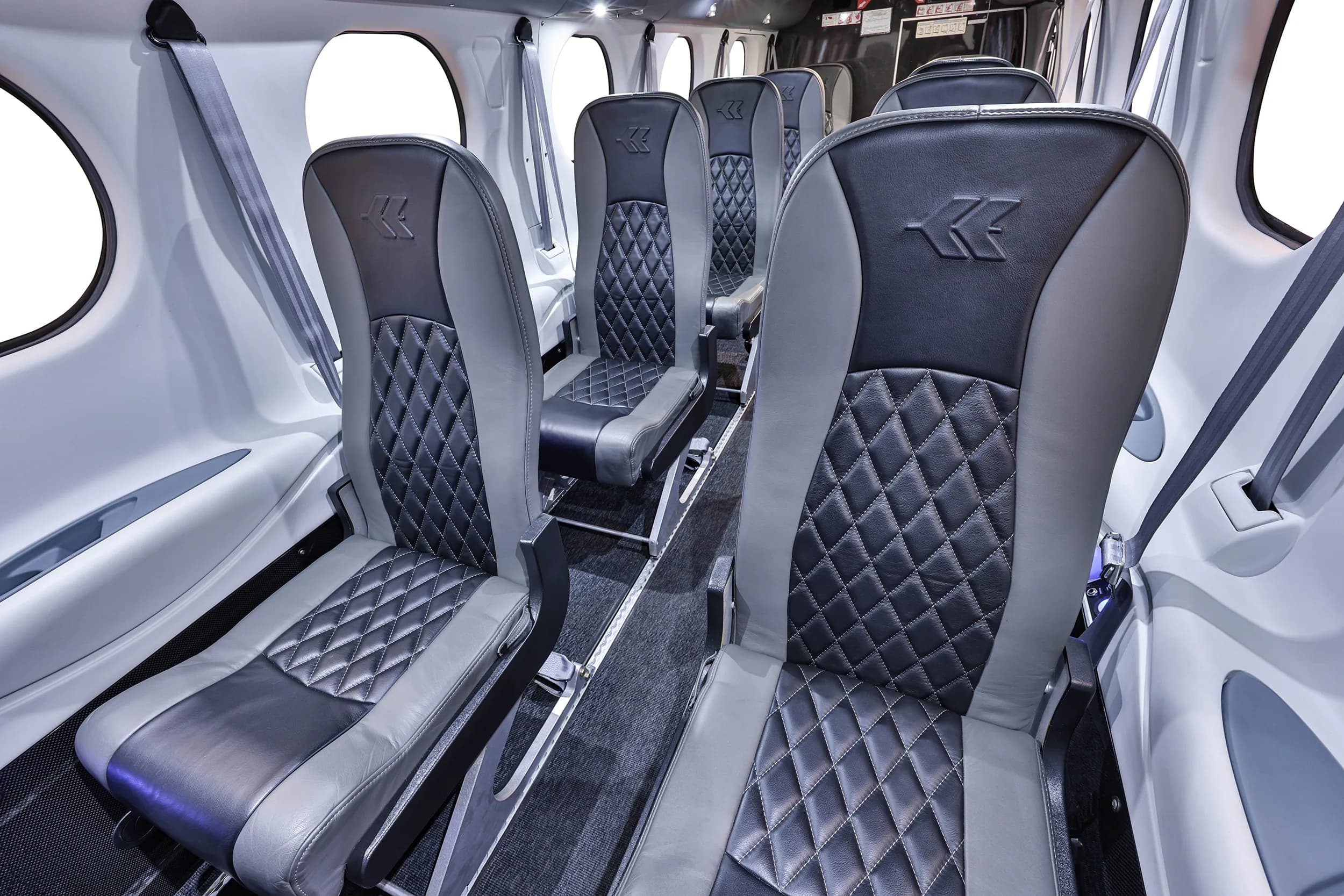 The aircraft cabin interior with multiple rows of grey and black quilted leather seats.